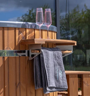 Close-up of wooden side tray with two pink champagne flutes and two grey towels on wood-fired hot tub exterior