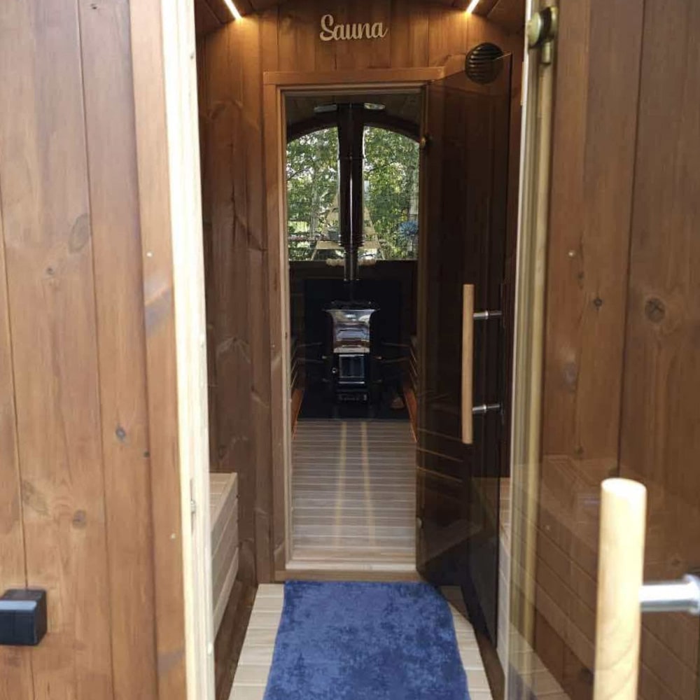 View through glass door into wooden sauna room with stove and blue floor mat at entrance