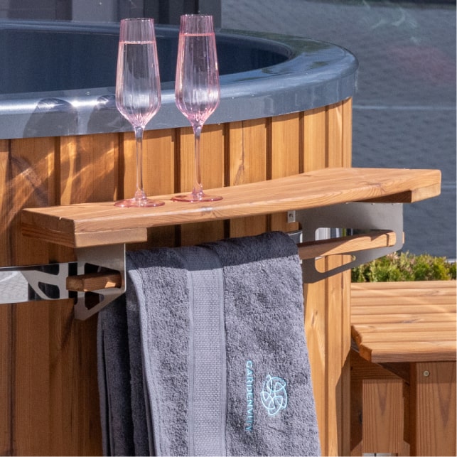 Close-up of wooden shelf attached to hot tub with two pink champagne flutes and a gray towel hanging below.