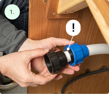 Close-up of hands assembling a black and blue connector on a grey flexible hose attached to wooden paneling