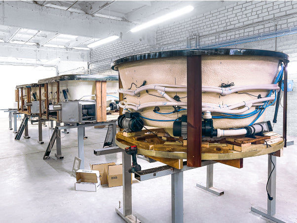 Interior view of a spacious workshop with multiple wood-fired hot tubs in assembly on metal stands and white brick walls