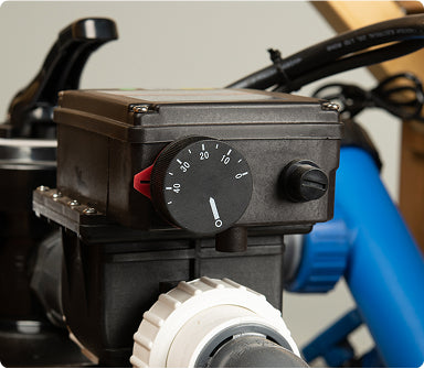 Close-up view of a black control box with a numbered dial and valve fittings on connected pipes in an indoor setting