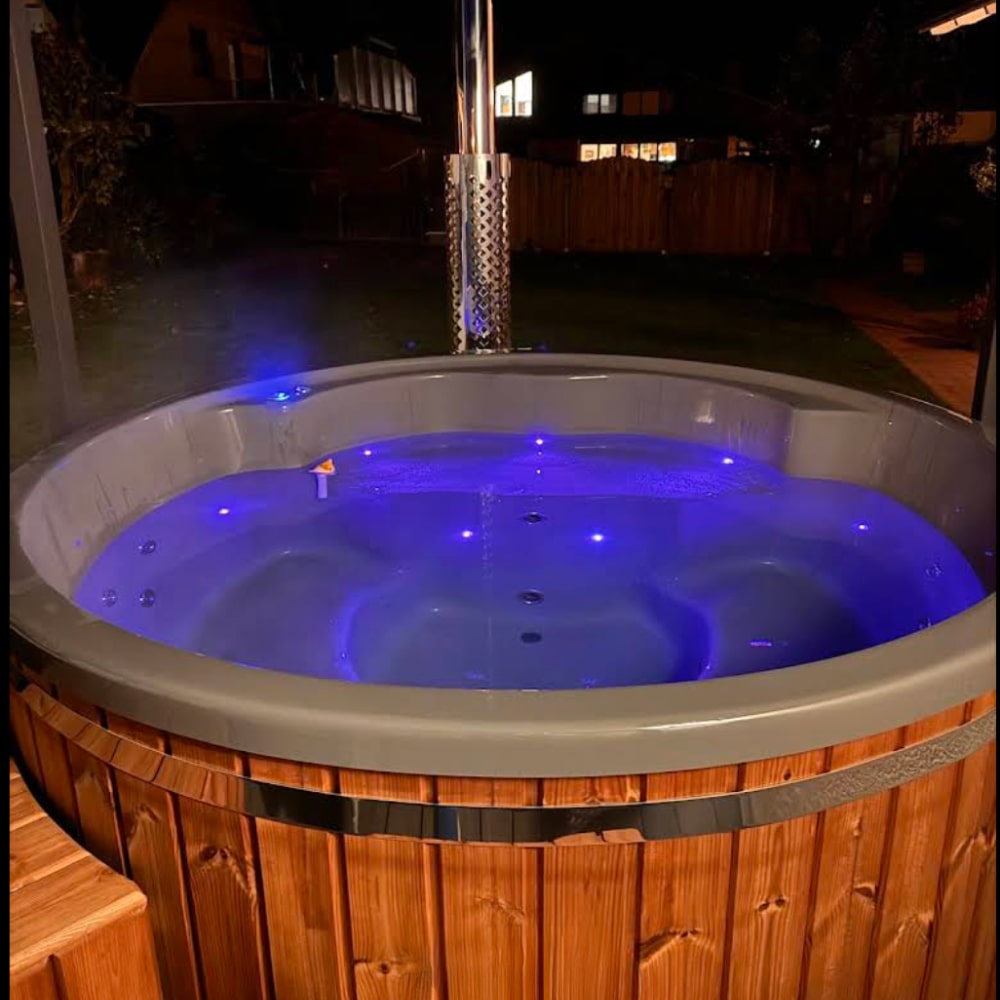 Customer photo of a wood-fired hot tub at night with blue LED lighting illuminating the water.