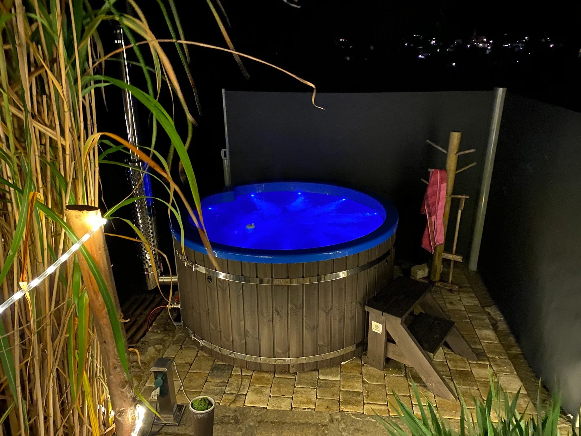 Gardenvity wood fired hot tub illuminated with blue LED lights on rustic stone patio