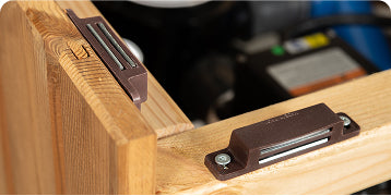 Close-up view of two brown magnetic catches mounted on wooden surfaces with screws.