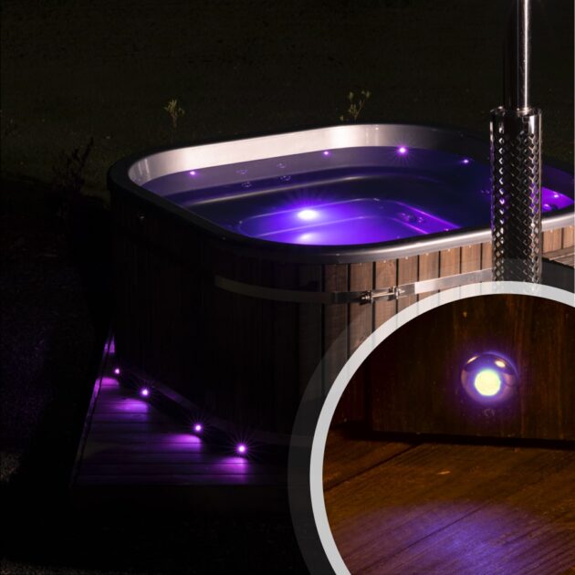 Wood-fired hot tub illuminated with purple LED lighting at night, highlighting underwater and exterior lights.
