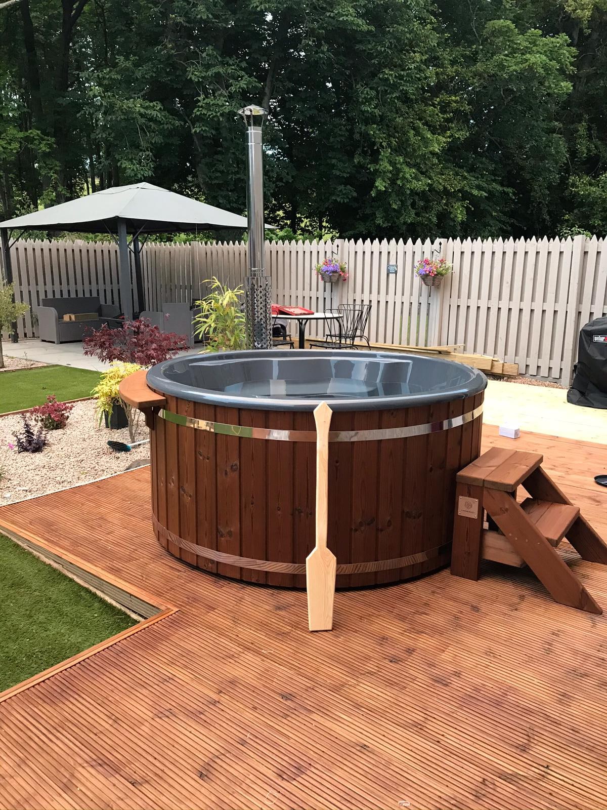 Gardenvity wood fired hot tub on wooden decking with outdoor umbrella and seating area.