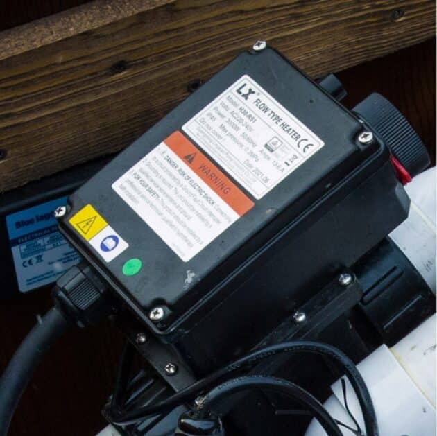 Hot tub electric heater control unit with safety labels and power connection installed inside the tub housing.