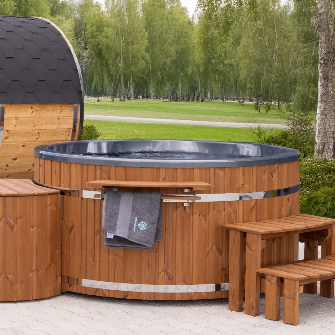 Outdoor view of wood fired hot tub with dark interior, wooden steps, towel rack, and hexagonal sauna cabin nearby