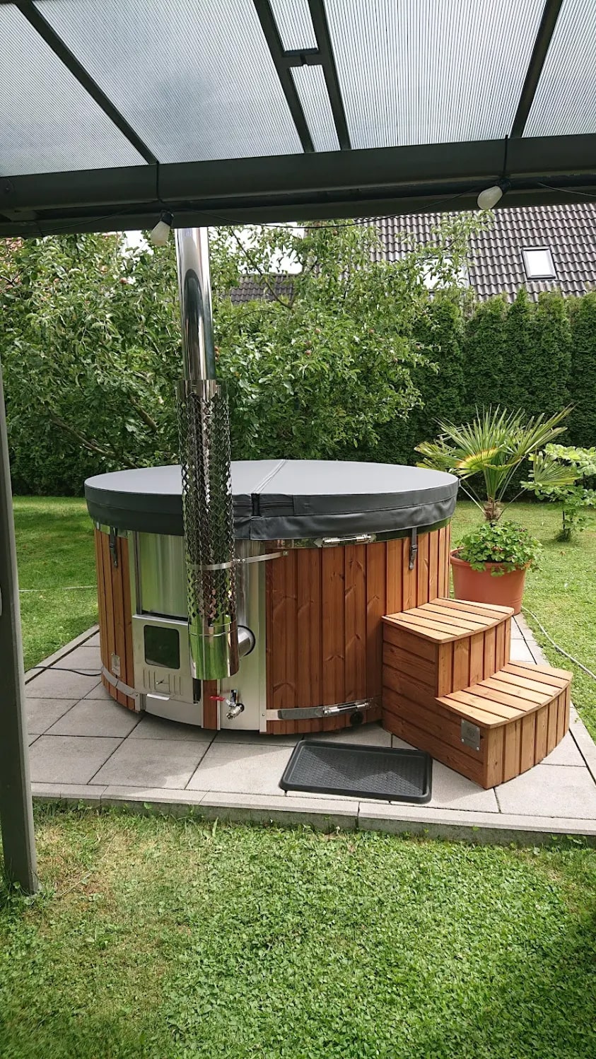 Compact Gardenvity wood fired hot tub placed under a terrace roof in a green backyard