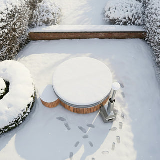 Top-down view of a snow-covered outdoor hot tub with wooden steps and a metal stove surrounded by snow and footprints